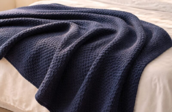 Organic cotton honeycomb jacquard blanket in deep navy blue draped across a bed with morning sunlight