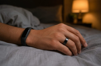 Smart ring on finger and fitness strap on wrist resting on gray bedsheet