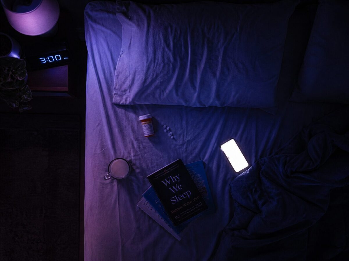 Sleeping pill bottle, glass of warm milk, clock showing 3am, sleep books and bright phone on bed in dim purple light representing sleep myths