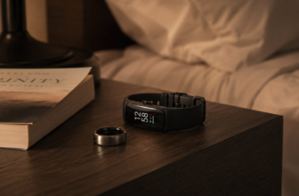Smart ring and fitness tracker watch on a wooden nightstand next to a small lamp and book