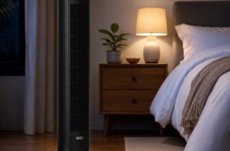 DREO black tower fan standing beside a bed in a dim bedroom with white linens