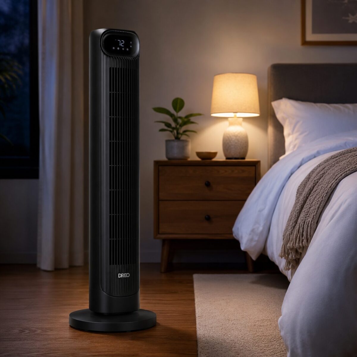 DREO black tower fan standing beside a bed in a dim bedroom with white linens