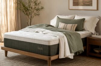 Queen hybrid mattress on a low wooden bed frame with white and sage bedding in soft morning light