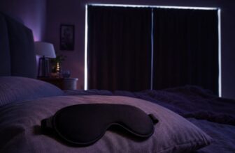Dark bedroom with blackout curtains on the window and a contoured sleep mask on the pillow
