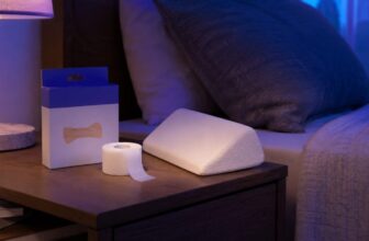 Nasal strips box, medical tape roll and foam wedge pillow on a nightstand in purple night lighting