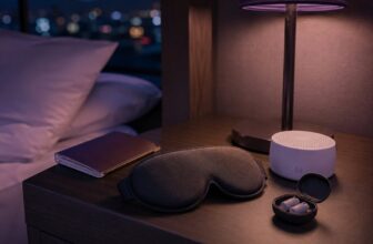 Sleep mask, white noise machine, and earplugs on a hotel nightstand with a passport